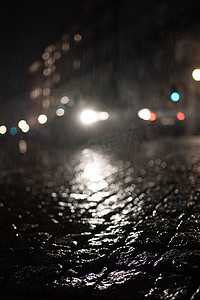 汽车前灯在雨中闪耀的模糊低视角与夜间湿鹅卵石的反射