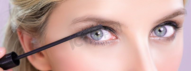 把卡摄影照片_特写美丽的女人把迷人的黑色睫毛膏放在长而浓密的睫毛上。