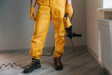 家杂摄影照片_穿着黄色制服的杂工，钻头站在室内。