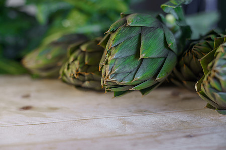 农民新鲜采摘的朝鲜蓟的刺叶特写放在木桌上，阳光、素食和地中海美食配料照亮