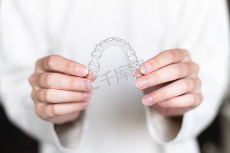宋代美学摄影照片_在模糊的背景下，一位女士手持隐形矫正器的特写，用于美白和矫正牙齿。