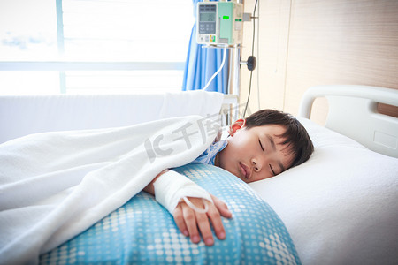 亚洲男孩躺在病床上，静脉注射盐水 (IV)。