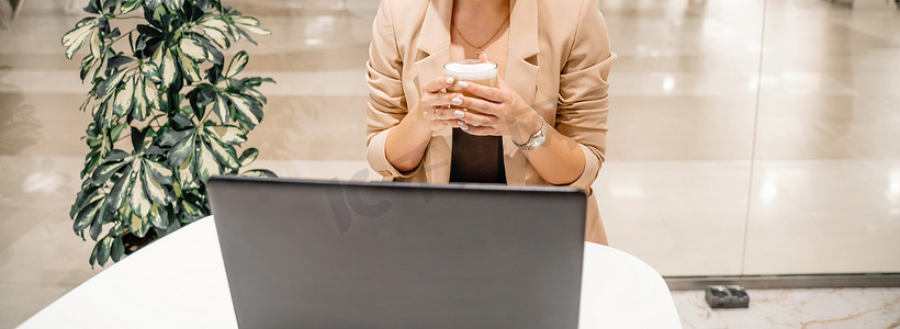 一位女商人坐在咖啡馆里，在电脑前工作，喝着咖啡。