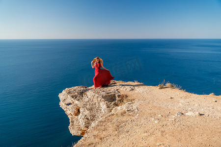 飘动摄影照片_在大海的映衬下，一位身着红色飞裙的女子在风中飘扬。