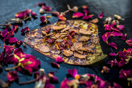 两人提水摄影照片_黑色表面上著名的印度传统马萨拉锅或 meetha 锅的特写，上面有一些玫瑰水，包括涂有 sauf、supari、甜味剂和一些椰子粉。