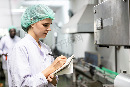 生产线摄影照片_质量控制和食品安全白人女工检查食品和饮料厂生产线的产品标准。