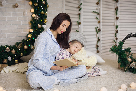 妈妈在圣诞树附近给可爱的小女儿读书
