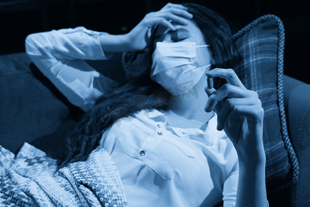 坐在沙发上的年轻女性，身上盖着一条毯子，冻得鼻涕直流，发烧、被抓、生病的女孩有流感症状、流感或病毒概念