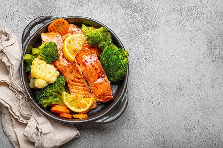 排班表模板摄影照片_健康的烤鱼鲑鱼排、西兰花、花椰菜、胡萝卜在灰色石头背景的黑色铸铁砂锅碗中。