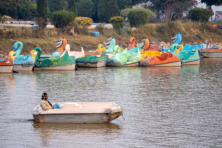 男子在地标性的苏赫纳湖上划着一艘破旧的脚踏船，远处停着其他船只，展示了在这个旅游胜地经营景点的人们的生活