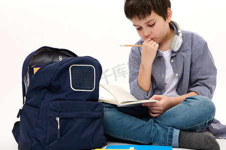 体贴的小学生思考学校项目，做作业，坐在书包旁，在白色背景中与世隔绝