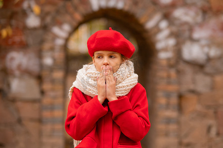 穿着红色外套和贝雷帽的白人女孩在秋天的公园散步时冻僵了。