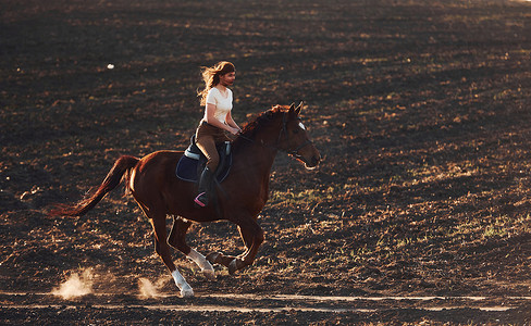 阳光明媚的白天，戴着防护帽的年轻女子在农田里骑马