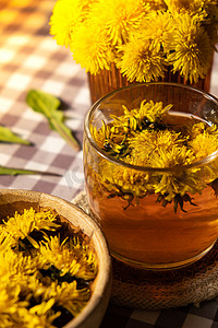中草药茶摄影照片_桌上玻璃杯中的蒲公英花健康茶。