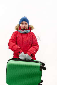 快乐的旅行者青春期男孩穿着温暖的红色羽绒服，拿着绿色手提箱，在白色背景中被隔离。