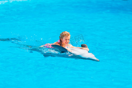 鲸鱼尾巴摄影照片_在海豚馆与海豚一起游泳的快乐小女孩