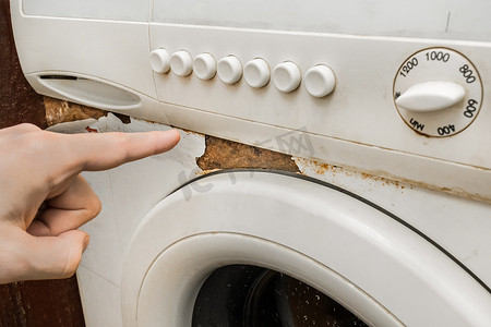 钙化摄影照片_一个男人的手指指向一台破旧洗衣机前键盘旁边的锈迹。