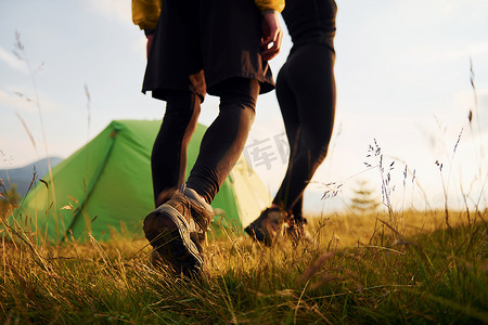 一对夫妇在绿色帐篷附近的户外散步。