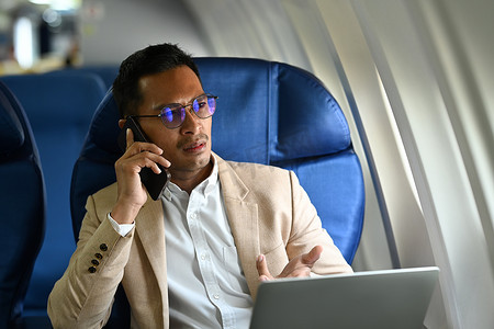 手机联系人摄影照片_忙碌的商人飞机乘客在商务旅行期间使用笔记本电脑和呼叫业务联系人