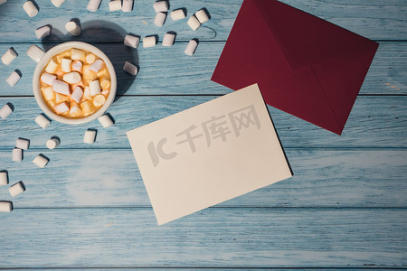贺卡或邀请卡模拟与红色信封与白杯咖啡和棉花糖在木制背景。