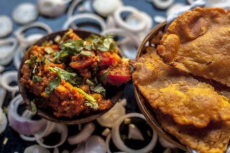土豆地摄影照片_Batate ki sukhi bhaji 或土豆 sabji 在粘土碗中的特写镜头，以及一些干燥的普通油炸 puri 和一些黑色表面上的切洋葱。