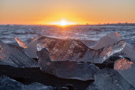 钻石海岸摄影照片_日落时在黑色火山沙滩上闪耀的纯冰。