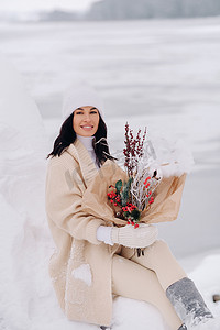 一个穿着米色开衫、开着冬花的女孩正坐在白雪皑皑的公园里的大自然中。