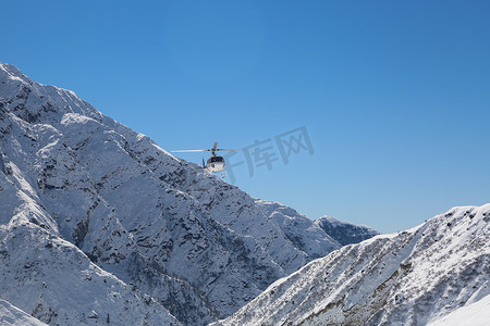 飞行中的直升机摄影照片_直升机在喜马拉雅山白雪覆盖的山谷中飞行。