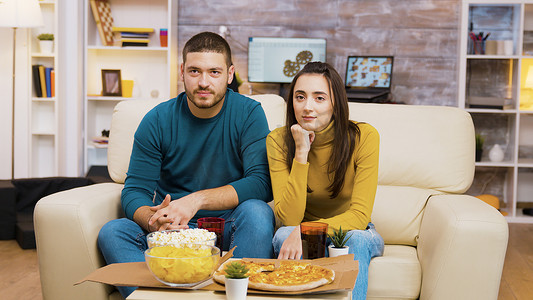 一对夫妇坐在沙发上边看电视边吃披萨边笑