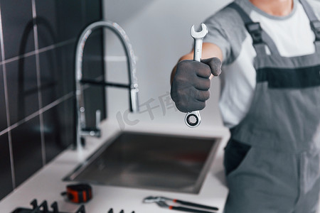 在厨房里手拿扳手的灰色制服年轻专业水管工的特写镜头
