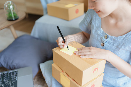 一家小型初创公司的肖像，中小企业老板，一位亚洲女企业家，正在记事本上写下信息以整理产品，然后将其包装到客户的内盒中