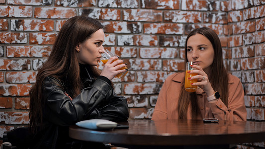 两个棕发女孩在咖啡馆里边喝果汁边聊天。