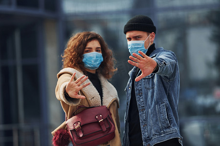 一对戴着防护面具的夫妇在检疫时间在商业大楼附近的城市户外散步。