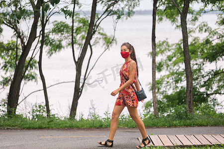 COVID-19 在城市中强制戴面具的妇女在城市公园夏季户外生活方式中戴着面具行走以预防冠状病毒。