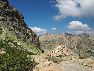 科西嘉阿尔卑斯山的高山风景，有绿色灌木和岩石桩石标，标有通往山顶罗通多山和白云蓝天的道路