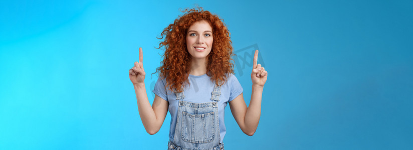 有动力的快乐开朗的红发愚蠢的卷发女人指着指数手指微笑迷人印象深刻兴奋显示令人敬畏的促销讨论有趣的广告蓝色背景