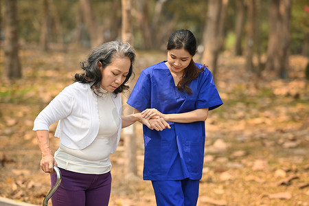 有爱心的女性看护者帮助老年妇女在公园散步的形象。