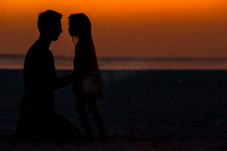 夕阳下的小女孩和爸爸剪影在海滩