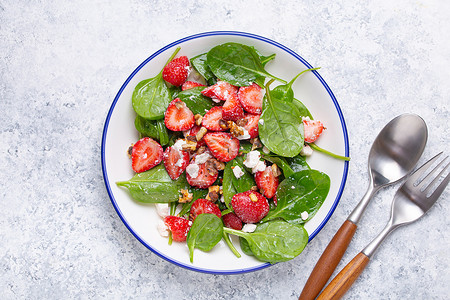 清淡健康的夏季沙拉，配以新鲜草莓、菠菜、奶油奶酪和核桃，放在白色陶瓷盘子上，上面是白色质朴的石头背景。
