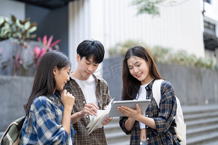 一群亚洲大学生在户外草地上阅读书籍和辅导特殊课程。