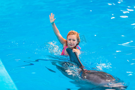 鲸鱼尾巴摄影照片_在海豚馆与海豚一起游泳的快乐小女孩