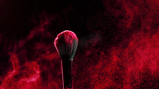 化妆刷与黑色背景上的红色粉末爆炸。