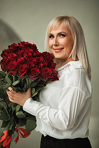 一位身穿白衬衫和黑裤子的时尚女性在室内摆着一束红玫瑰