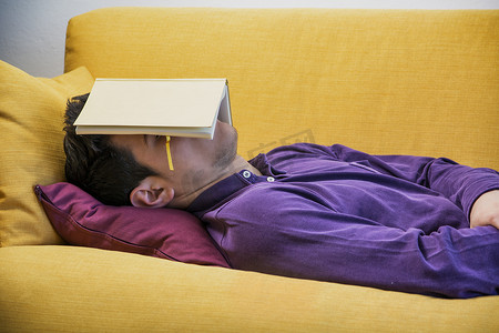 在家睡在书下的劳累过度、疲惫的年轻人