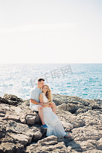 石子摄影照片_坐在海边岩石上的男人从后面抱着一个女人