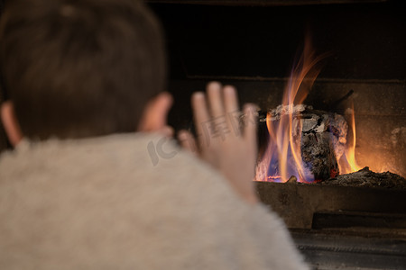 冬天柴火前裹着毯子暖手的小男孩的后视图