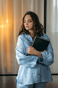 手里拿着平板摄影照片_一个穿着浅蓝色西装的年轻女子的画像站在房间里，手里拿着平板电脑和笔记本。