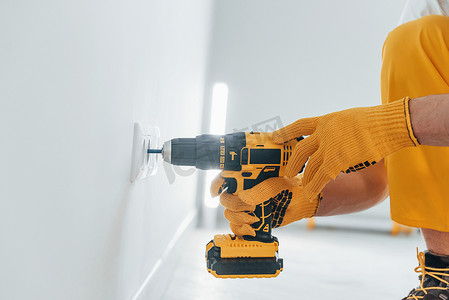 家杂摄影照片_黄色制服的杂工使用自动螺丝刀用电和安装新插座。