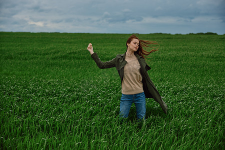 一位女士站在多云天气和强风中的田野中，她举起手面对镜头