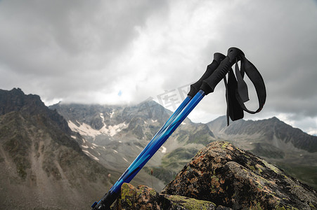 徒步背景摄影照片_夏季，在白雪皑皑的落基山脉的背景下，登山杖特写，躺在一块长满草的石头上
